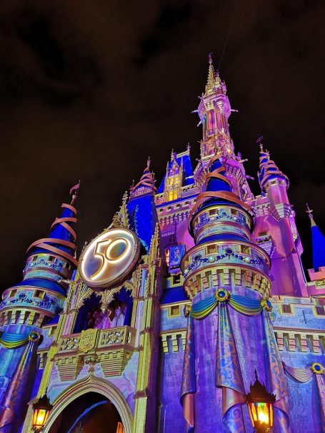 Illuminated Cinderella's castle at Magic Kingdom with vibrant lights against a night sky.