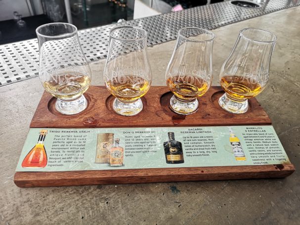 Four whisky tasting glasses on a wooden board with informational text beneath.