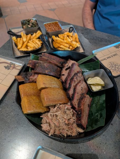 A platter featuring various meats, fried plantains, and sides of fries and dipping sauces.