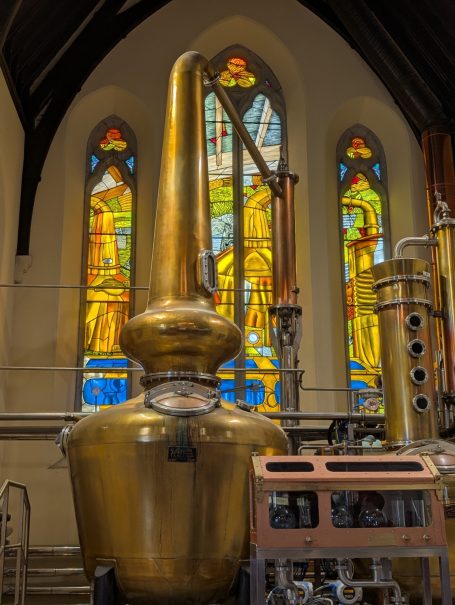 Copper distilling apparatus with stained glass windows in the background.