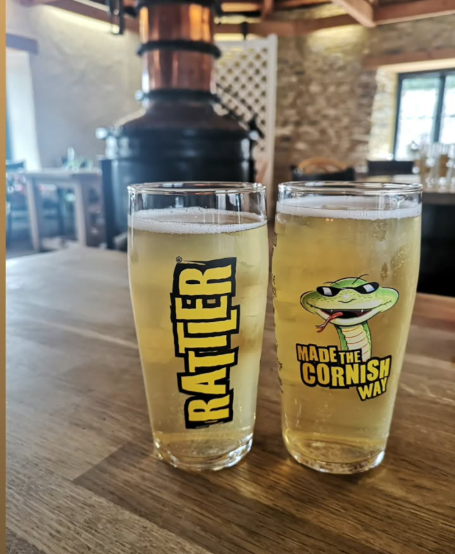 Two glasses of Rattler Cider on a wooden table in the bar area at Healey's Cornish Cyder Farm.