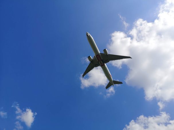 An Emirates A380 airplane flying high against a bright blue sky with fluffy white clouds out of Birmingham Airport.
