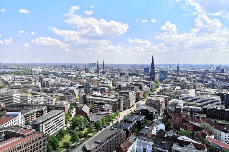 Panoramic view of a Hamburg skyline with buildings and spires under a blue sky with clouds.