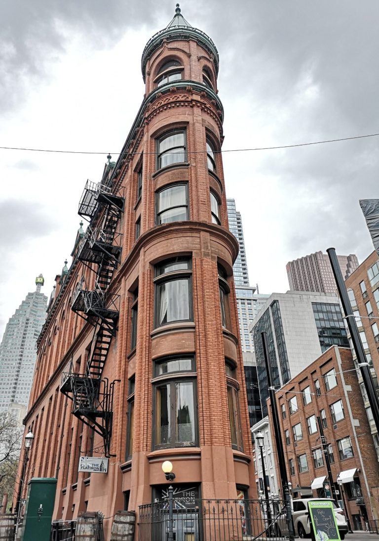 Reshaped brick building, known as the Gooderham Building with a rounded tower, set against modern skyscrapers located in Toronto
