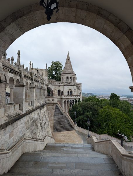View of Fisherman's Bastion in Budapest, framed by an archway, surrounded by greenery.