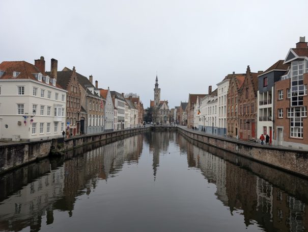 Canal scene in Bruges, Belgium, with historic buildings lining the banks on a misty day.