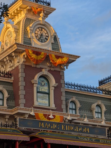 Clock tower with decorative elements and a banner, set against a blue sky. Located at Walt Disney's Magic Kingdom.