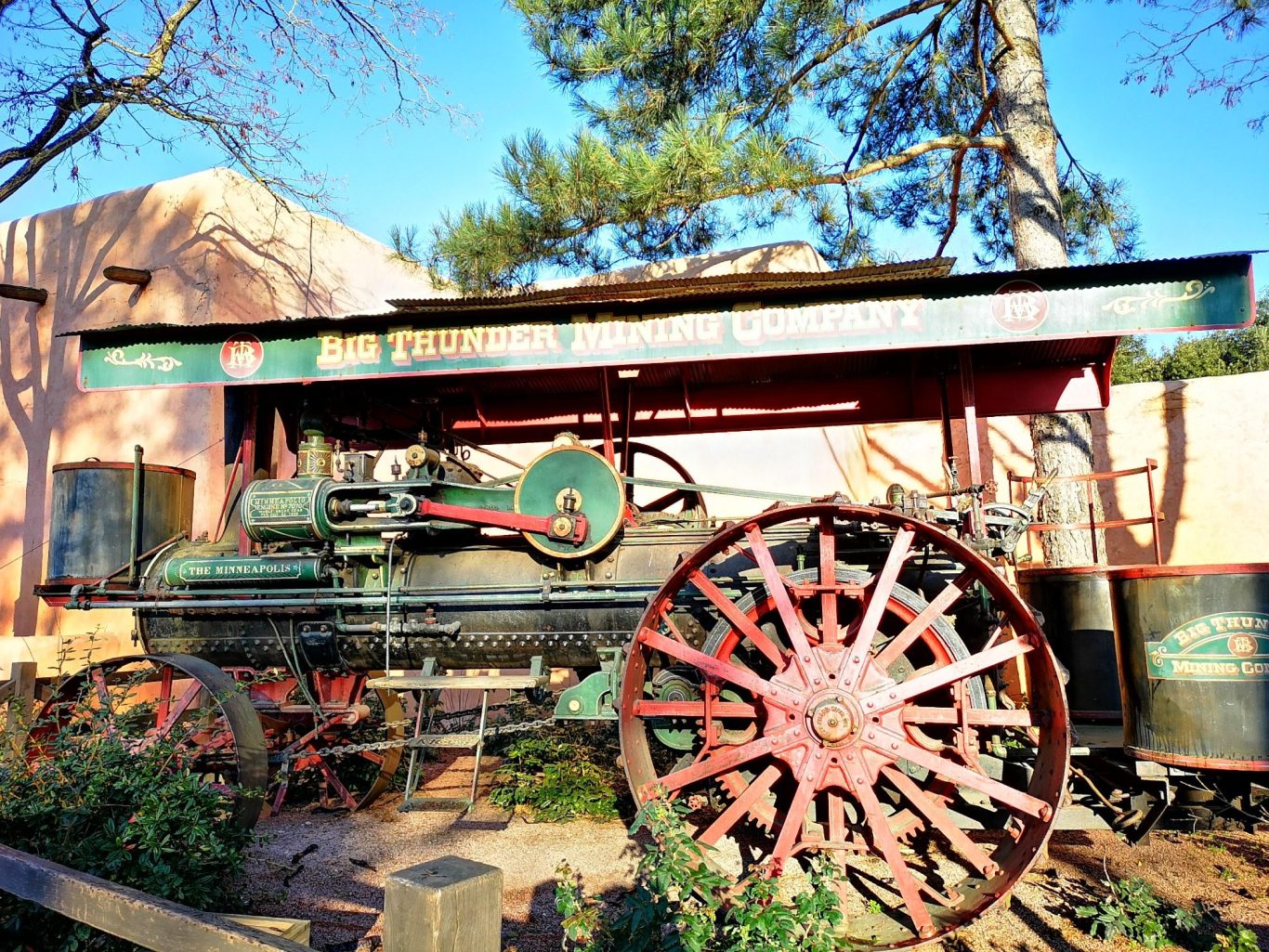Historic steam engine with large wheels, set against a blue sky and greenery.