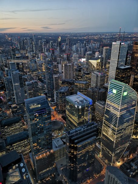Aerial view of a city skyline at dusk, with buildings and lights illuminating the streets.