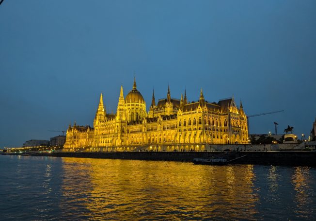 Illuminated Hungarian Parliament building reflecting on the Danube River at dusk.